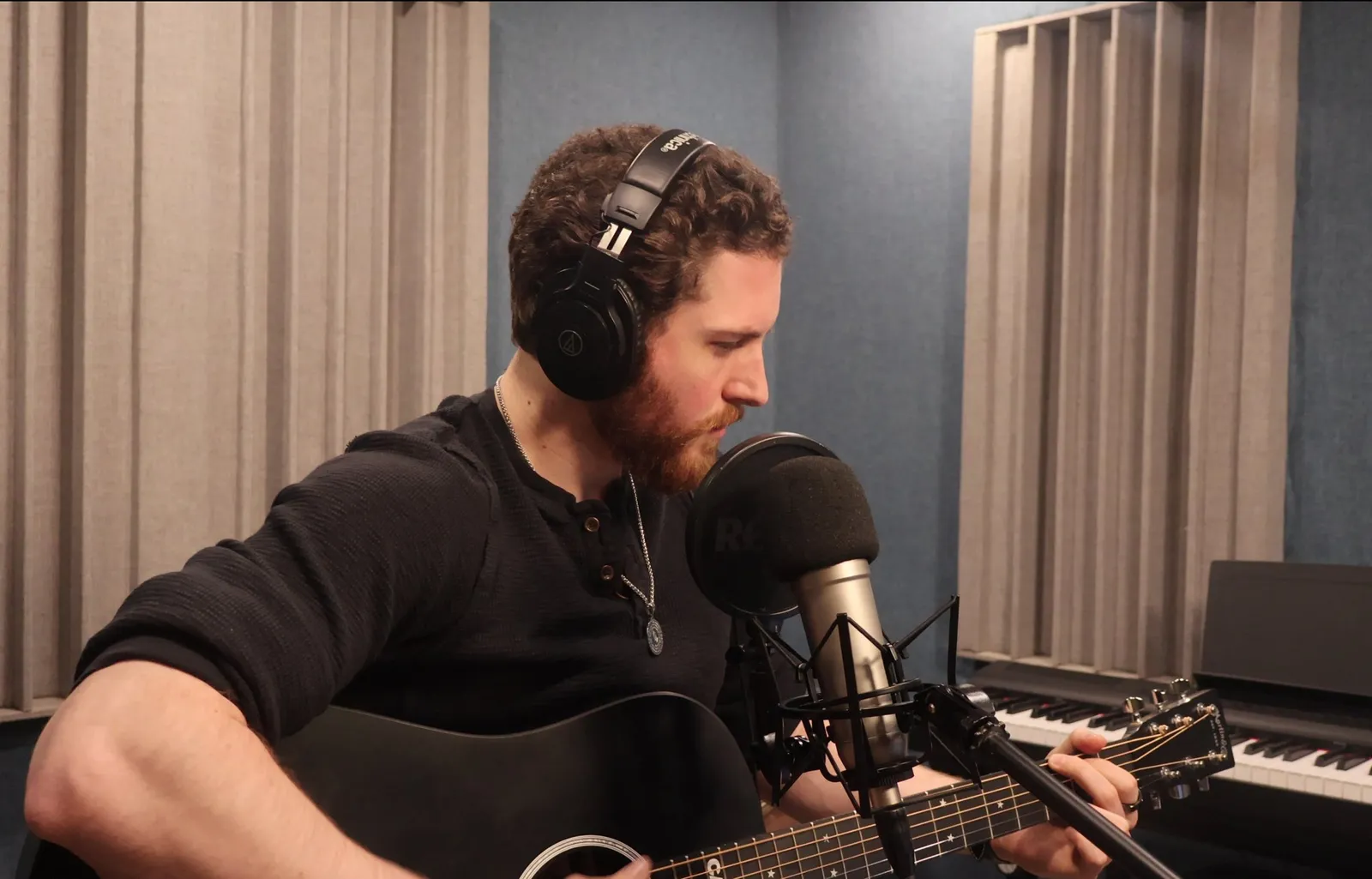 John Matthew Gillen in headphones, singing into a studio microphone while playing acoustic guitar